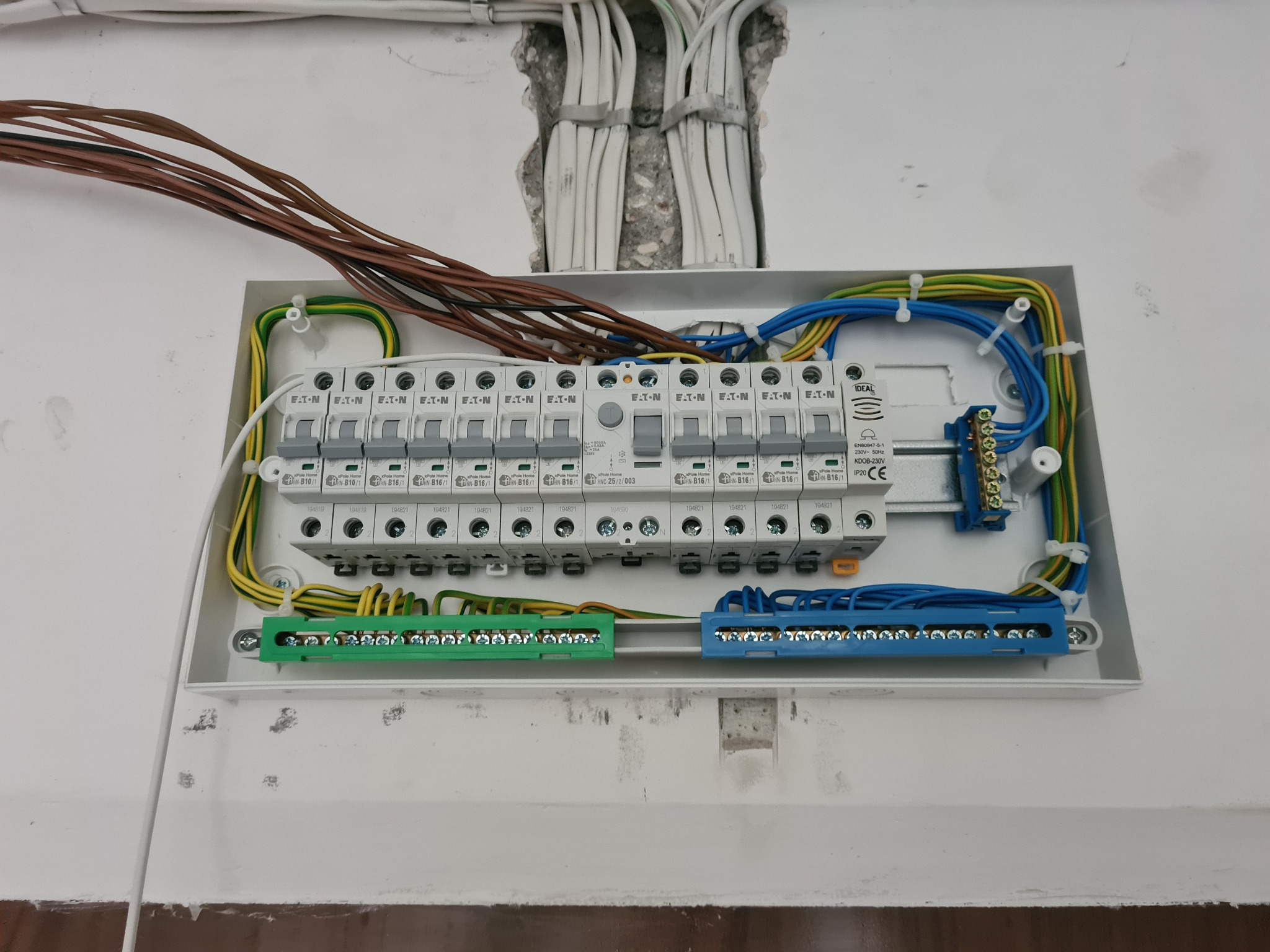Otwarta skrzynka elektryczna z bezpiecznikami EATON, widoczne przewody w różnych kolorach i listwy zaciskowe, instalacja w trakcie montażu.