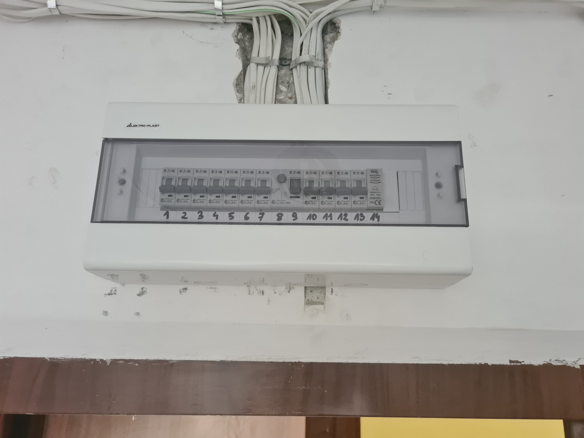 Rozdzielnica elektryczna firmy Elektro-Plast z czternastoma bezpiecznikami Eaton, zamontowana na ścianie z widocznymi przewodami wchodzącymi od góry.