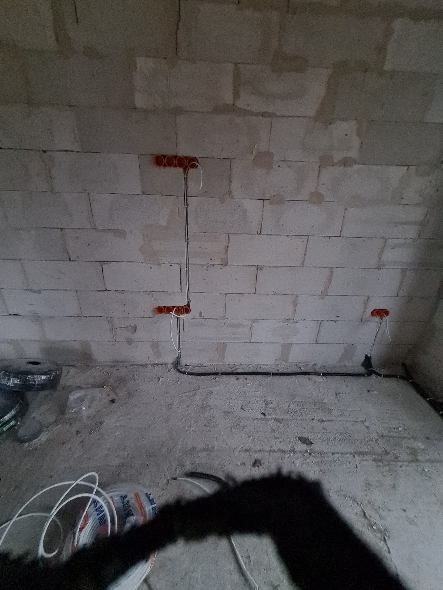 Surowy stan instalacji elektrycznej w nowym budynku: widoczne kable w peszlach i puszki instalacyjne w ścianie z betonu komórkowego, kable na podłodze.
