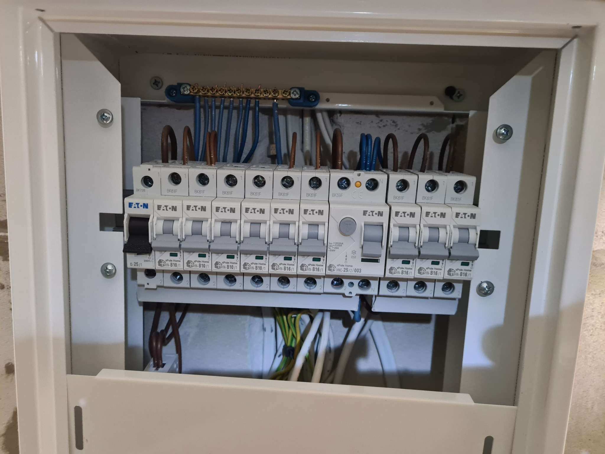 Otwarta skrzynka elektryczna z zamontowanymi bezpiecznikami EATON, widoczne przewody podłączone do listwy zaciskowej i dolnej części bezpieczników.