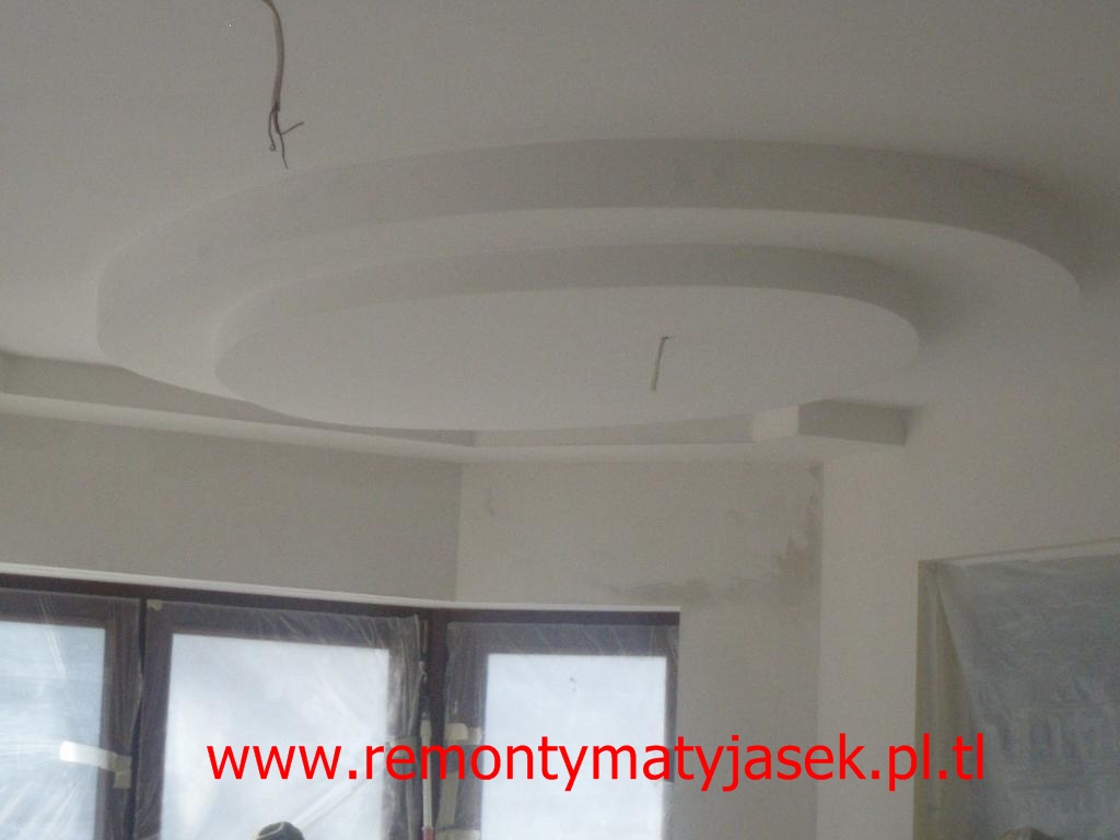 Wykończony sufit podwieszany z okrągłym elementem dekoracyjnym i wystającym przewodem elektrycznym, ściany przygotowane pod malowanie.