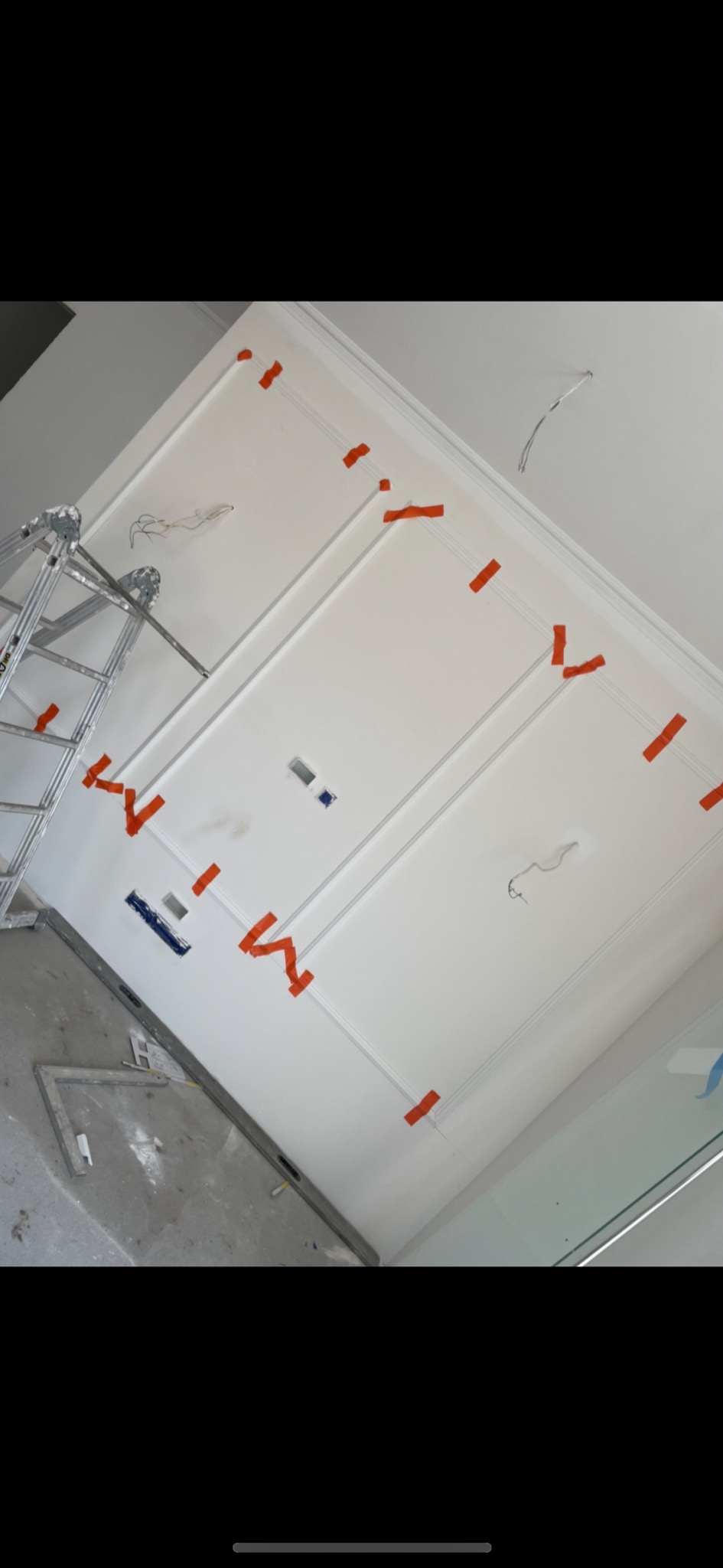 Biały sufit z dekoracyjnymi listwami i pomarańczową taśmą maskującą, widoczna drabina i narzędzia na podłodze, w trakcie prac wykończeniowych.