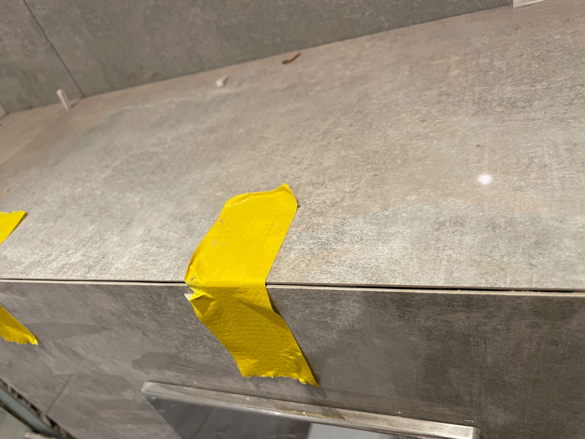Szare płytki ceramiczne zabezpieczone żółtą taśmą malarską podczas prac wykończeniowych.