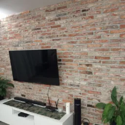 Ściana z cegły klinkierowej jako element dekoracyjny wnętrza, z zawieszonym telewizorem i białym stolikiem RTV, dekoracyjna bieżnik na szafce RTV.