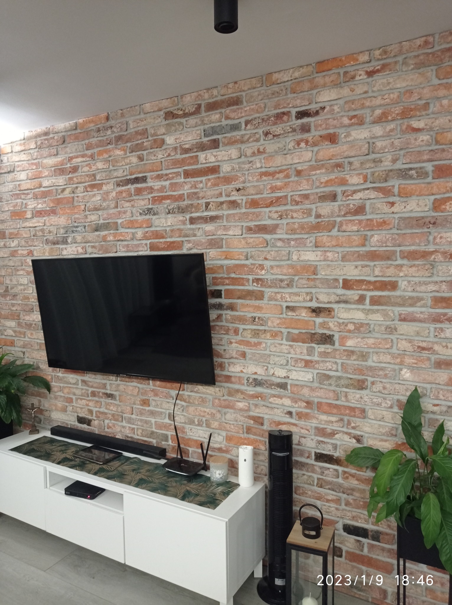 Ściana z cegły klinkierowej jako element dekoracyjny wnętrza, z zawieszonym telewizorem i białym stolikiem RTV, dekoracyjna bieżnik na szafce RTV.