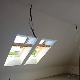 Poddasze po szpachlowaniu i malowaniu z dwoma oknami dachowymi, widoczne przewody elektryczne wystające z sufitu.