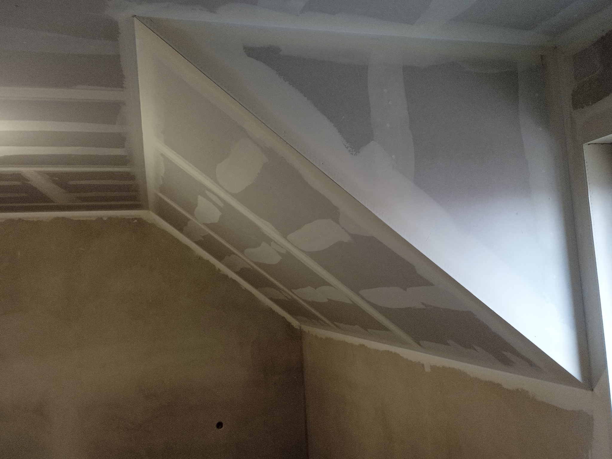 Skośny sufit z płyt kartonowo-gipsowych w trakcie szpachlowania, widoczne łączenia płyt i ślady szpachli.