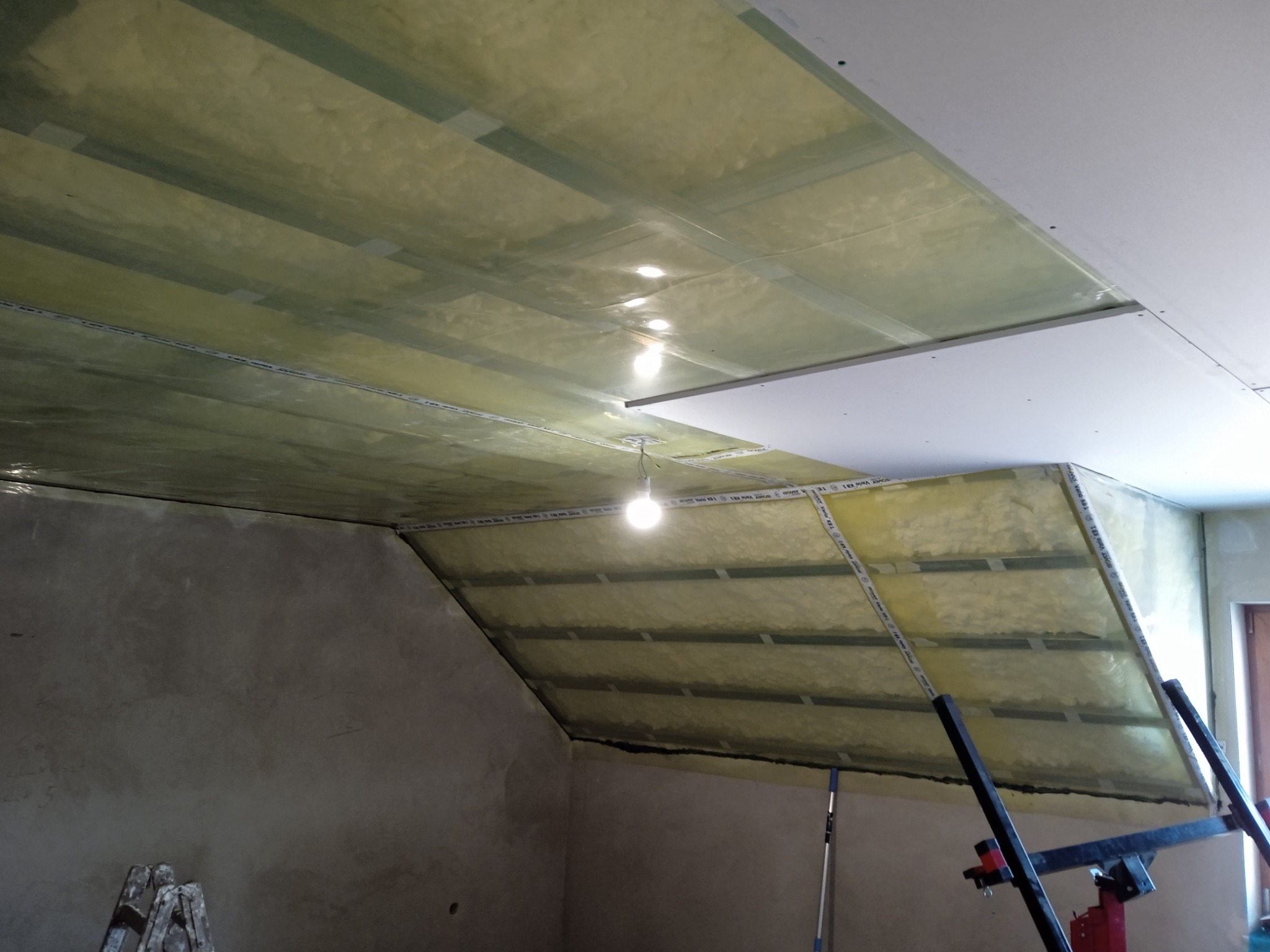 Montaż izolacji i płyt gipsowo-kartonowych na poddaszu w Łomży, widoczne profile konstrukcyjne i oświetlenie robocze.