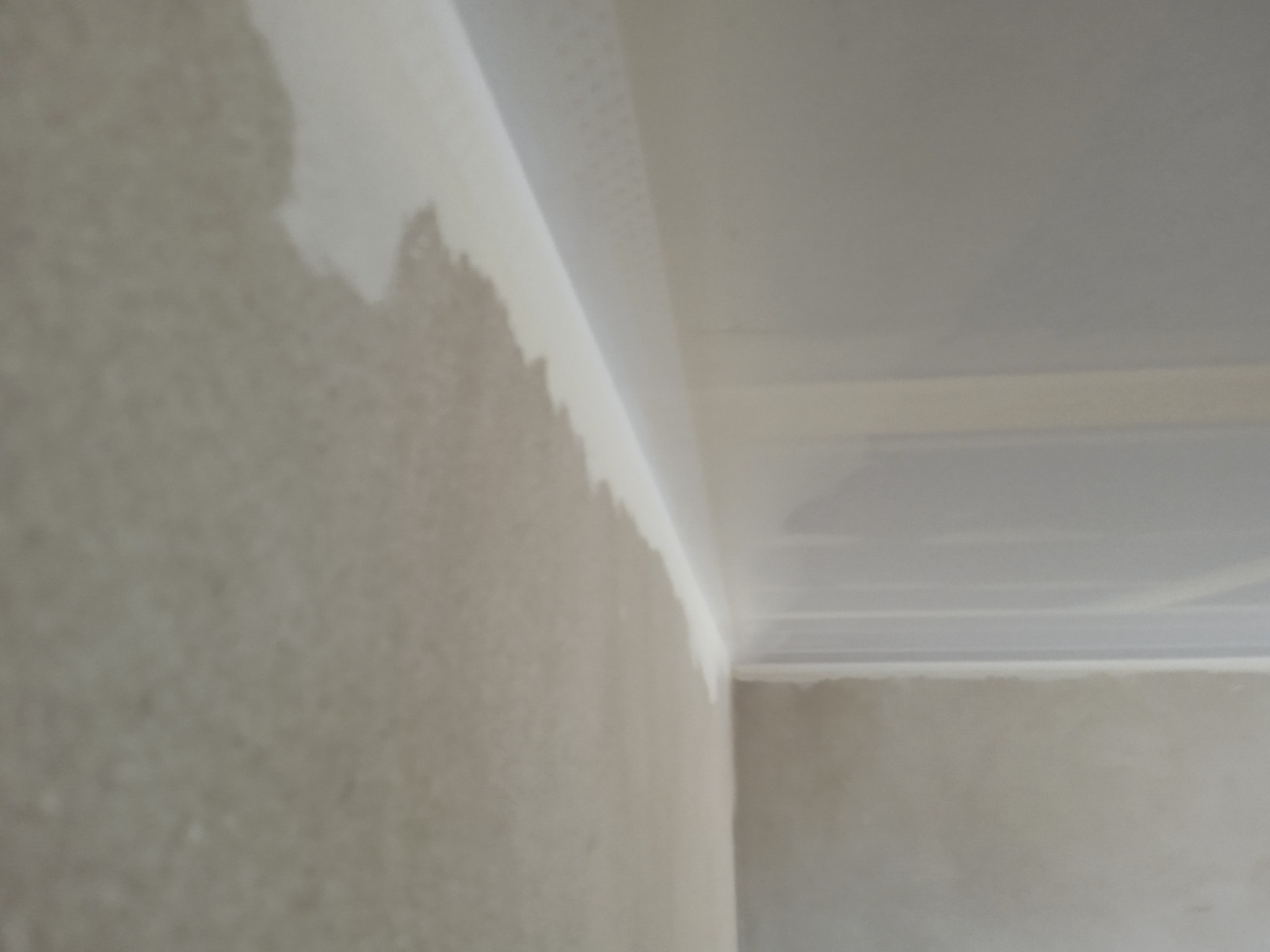 Narożnik pomieszczenia w trakcie prac wykończeniowych, widoczna surowa ściana ze śladami szpachli na łączeniu z sufitem podwieszanym z płyty gipsowej.