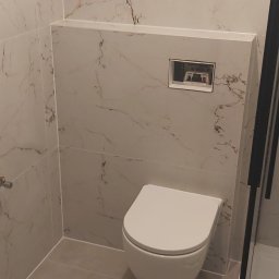 Kamil Kamiński - Nowoczesna toaleta podwieszana w łazience wykończonej płytkami imitującymi marmur z ukrytym systemem spłukiwania za ścianą.