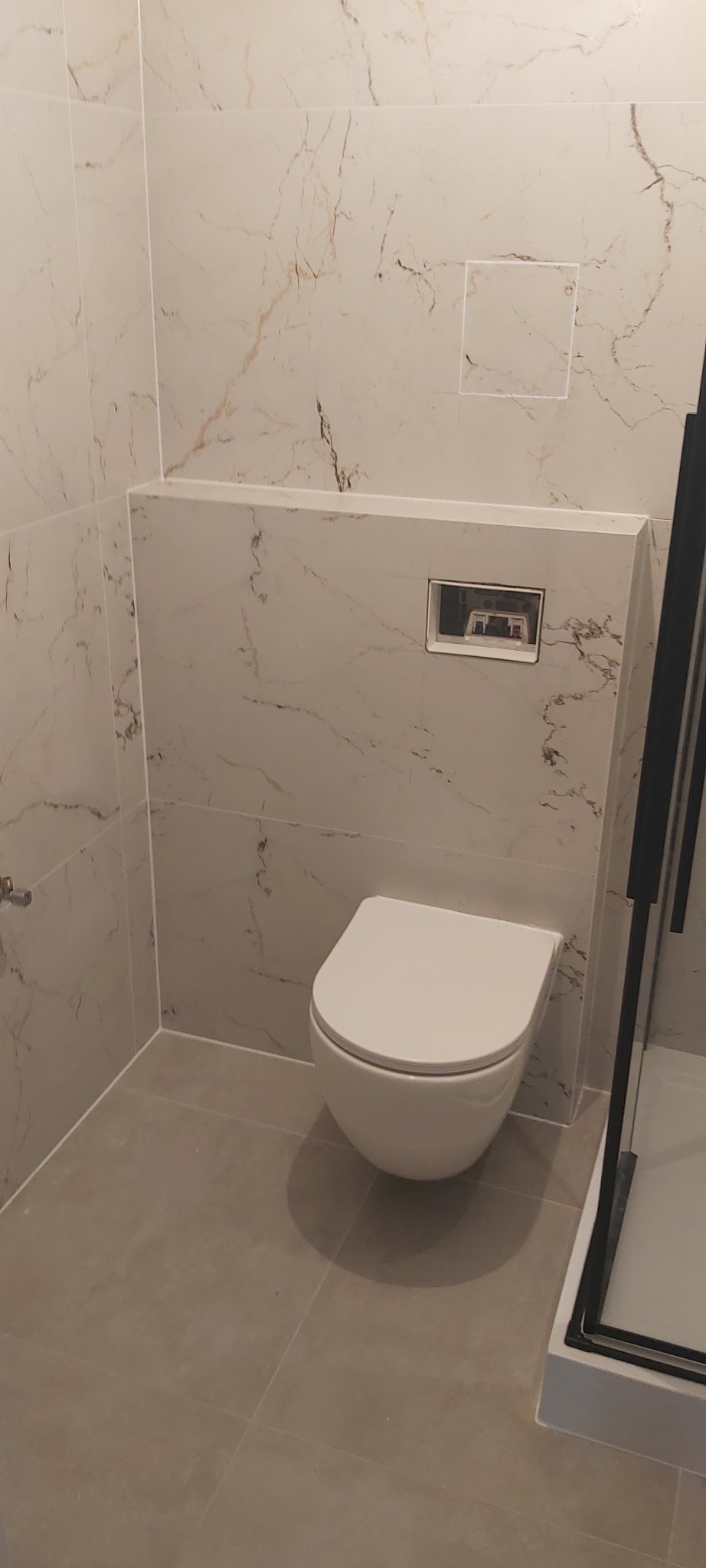 Nowoczesna toaleta podwieszana w łazience wykończonej płytkami imitującymi marmur z ukrytym systemem spłukiwania za ścianą.