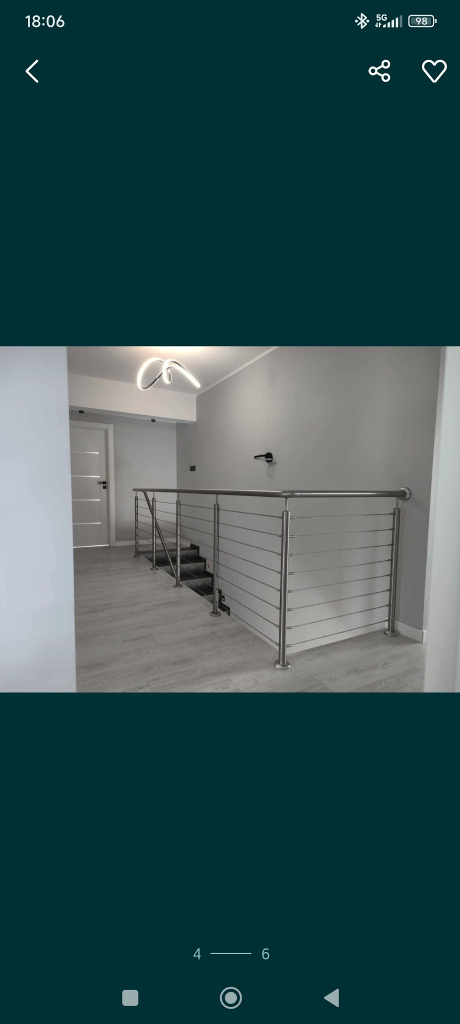 Wnętrze domu z metalową balustradą linkową na schodach. Widoczne schody z szarego kamienia, białe ściany i drzwi. Minimalistyczny design, nowoczesne oświetlenie.