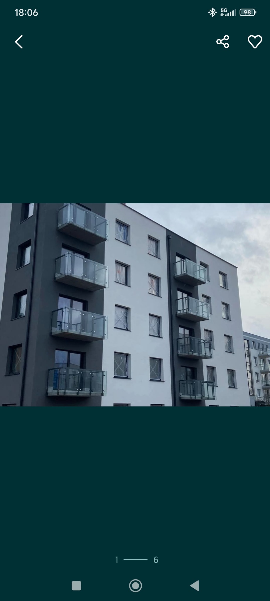 Nowoczesny budynek wielorodzinny z szarymi i białymi elewacjami, z balkonami zabezpieczonymi szkłem, uchwycony w pochmurny dzień.