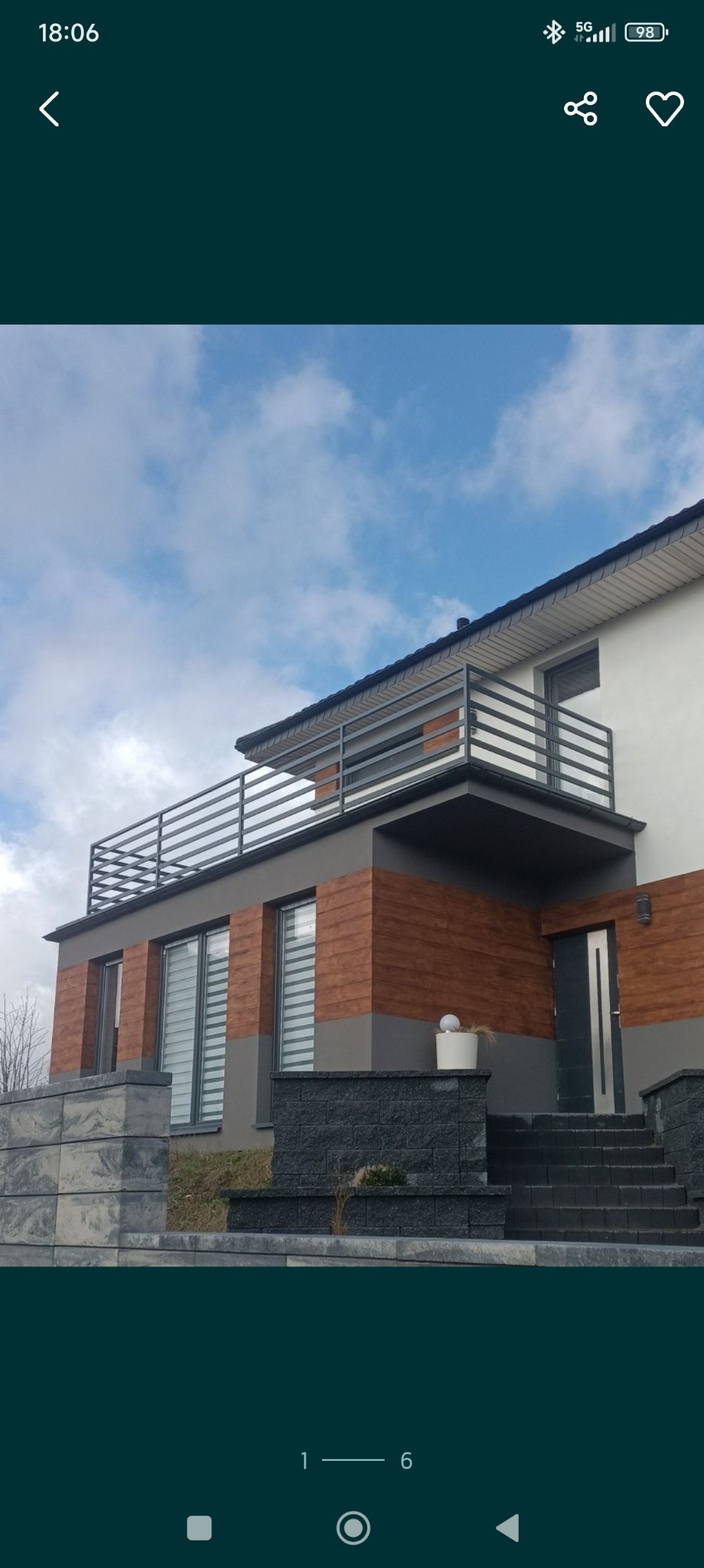 Nowoczesny dom z balkonem zabezpieczonym poziomą, szarą balustradą. Elewacja z elementami imitującymi drewno. Schody wejściowe wyłożone ciemną kostką.