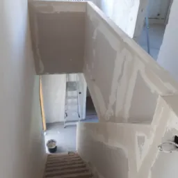 Schody w trakcie wyrównywania ścian gładzią w Grudziądzu, widoczny kubeł z masą szpachlową i drabina w tle.