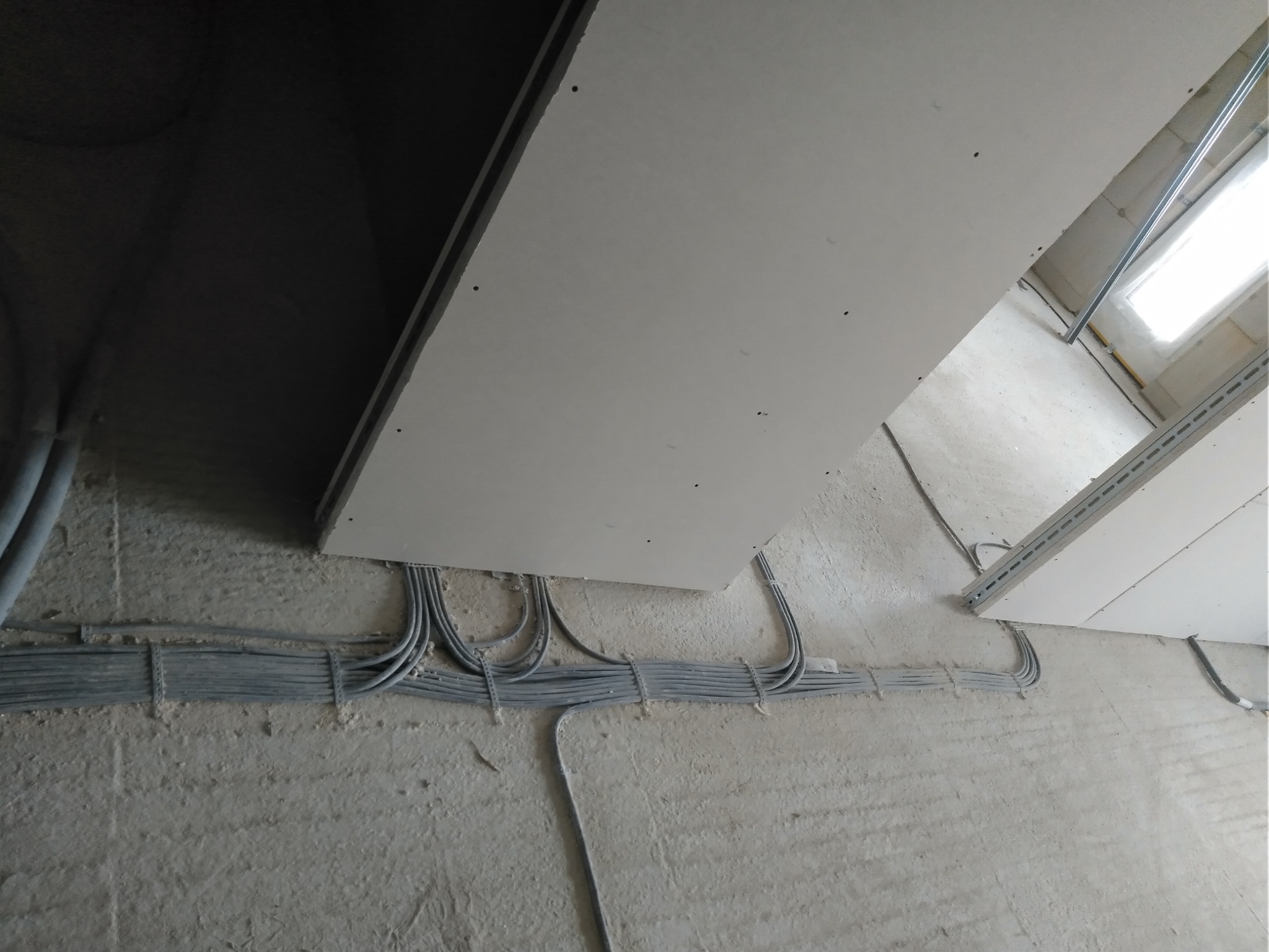 Szare kable elektryczne prowadzone pod płytą gipsową na ścianie w surowym wnętrzu podczas prac wykończeniowych. Widok z dołu.