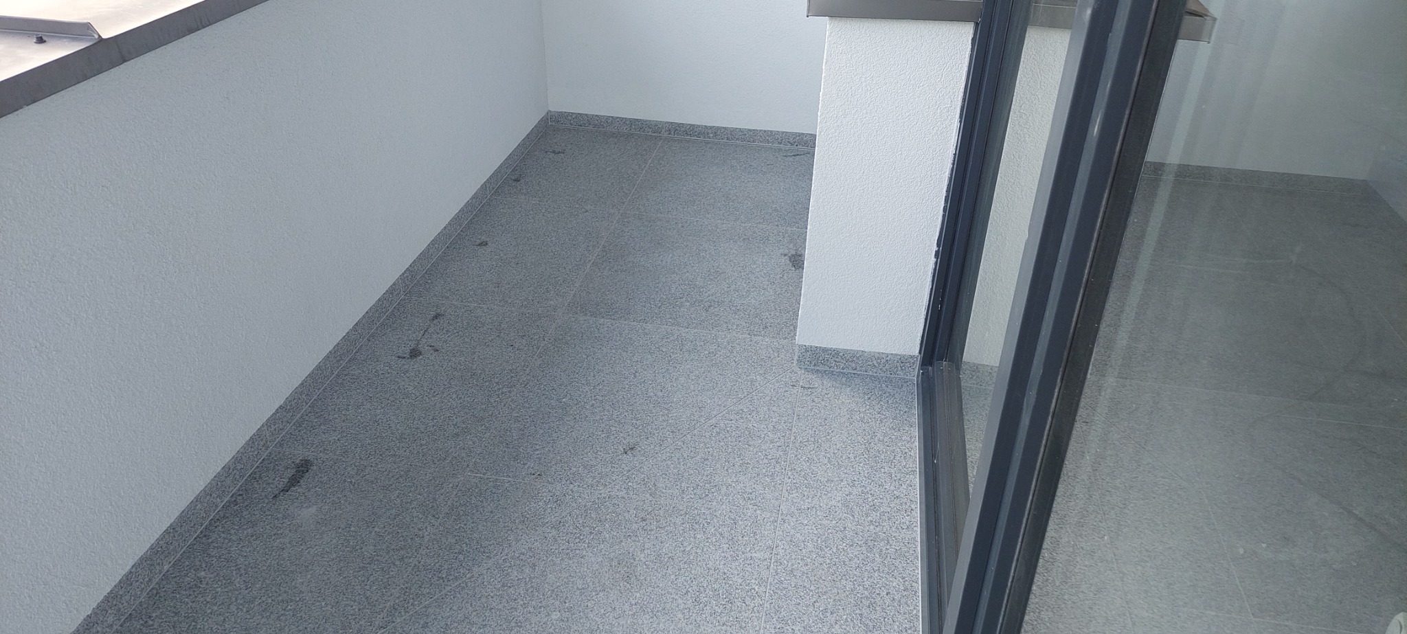 Wykończony balkon z szarymi płytkami podłogowymi i ścianami pomalowanymi na biało, widoczne ślady po fugowaniu.