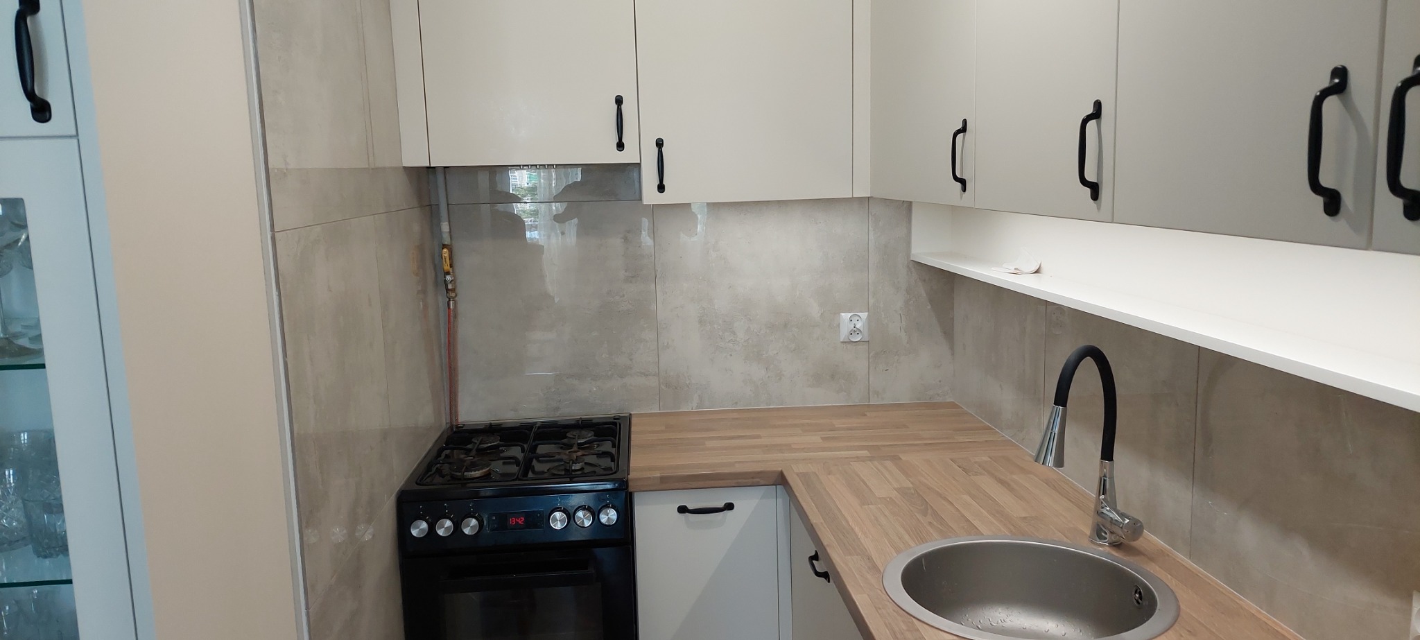 Nowoczesna kuchnia z beżowymi płytkami imitującymi kamień, drewnianym blatem i czarną armaturą, widok na płytę gazową.