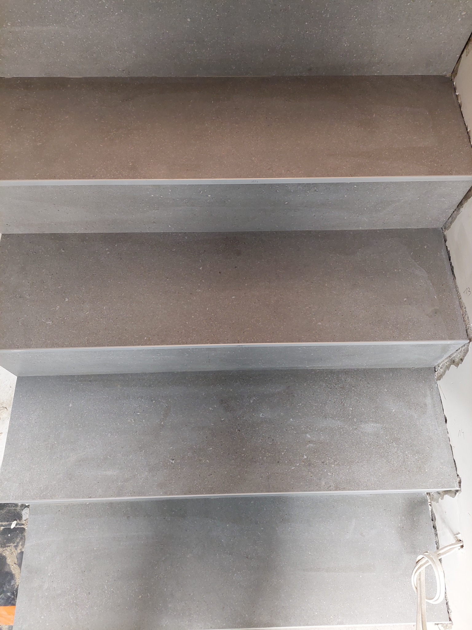 Ułożone płytki gresowe imitujące kamień na schodach wewnętrznych, widoczne niedokończone wykończenia ścian.