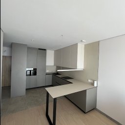 Inside Home Building - Nowoczesna kuchnia w odcieniach szarości, z wyspą i minimalistycznym oświetleniem. Widoczne płytki podłogowe imitujące drewno i kamień. Ujęcie z perspektywy.