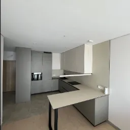 Nowoczesna kuchnia w odcieniach szarości i beżu, z minimalistycznym oświetleniem i wyspą z czarnymi nogami. Widoczne płytki podłogowe w dwóch kolorach.