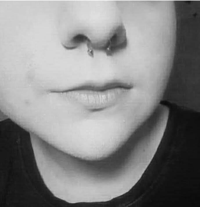 Czarno-białe ujęcie fragmentu twarzy z kolczykiem typu podkowa w przegrodzie nosowej.