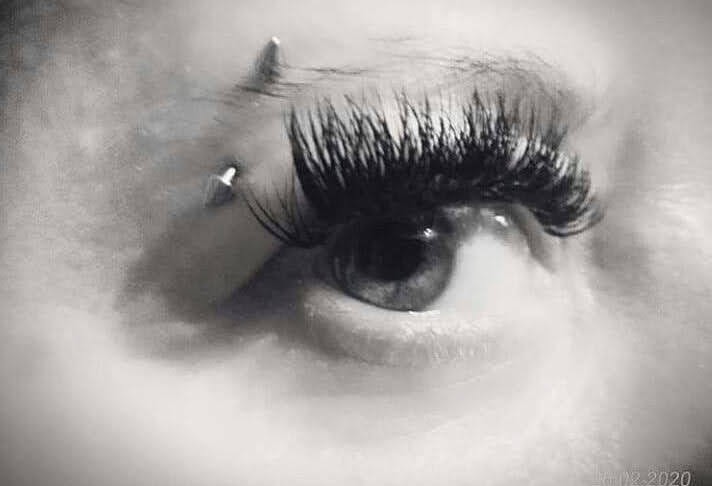 Czarno-białe zbliżenie na oko z przedłużonymi rzęsami i piercingiem brwi, uchwycone z bliska.