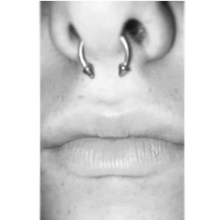 Czarno-białe zbliżenie twarzy z kolczykiem typu septum w nosie.