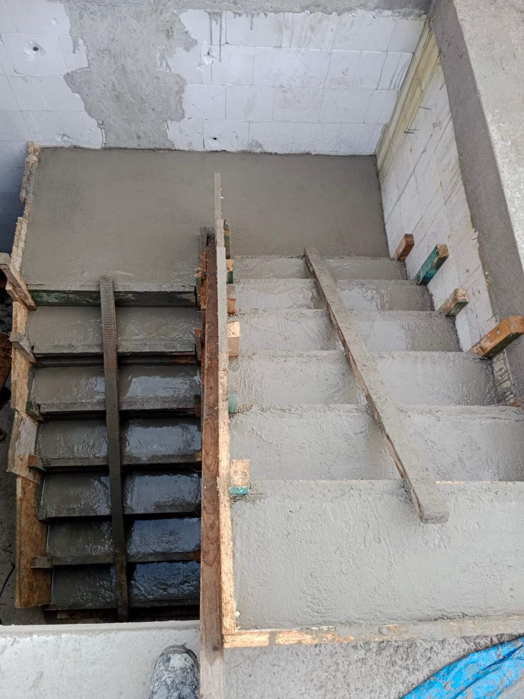 Wylewanie betonowych schodów wewnętrznych z drewnianym szalunkiem, widok z góry, surowy stan.