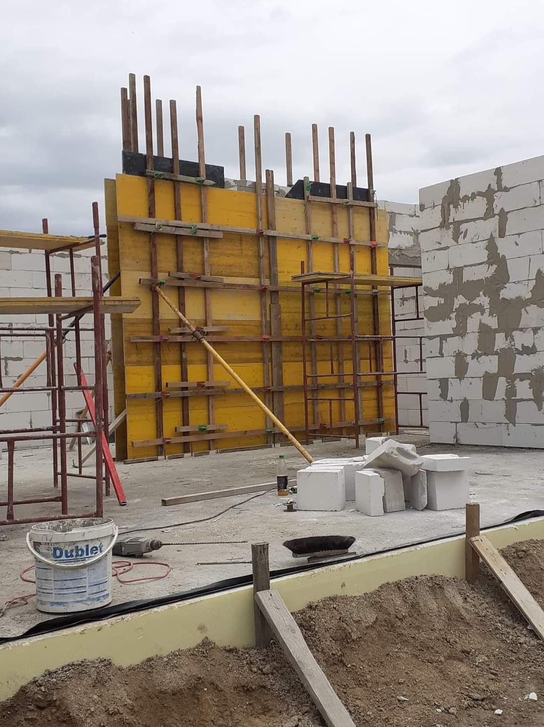 Żółte szalunki pod budowę ścian z betonu komórkowego, widoczne rusztowania, narzędzia i wiadro po farbie.