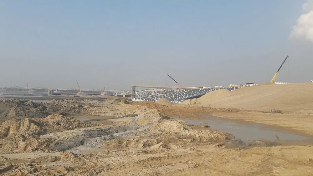 Budowa mostu z widocznymi dźwigami i ziemnym terenem w słoneczny dzień.