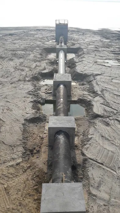 Długa rura na betonowych podporach, biegnąca przez piaszczysty teren. Na końcu konstrukcji widoczna osoba.