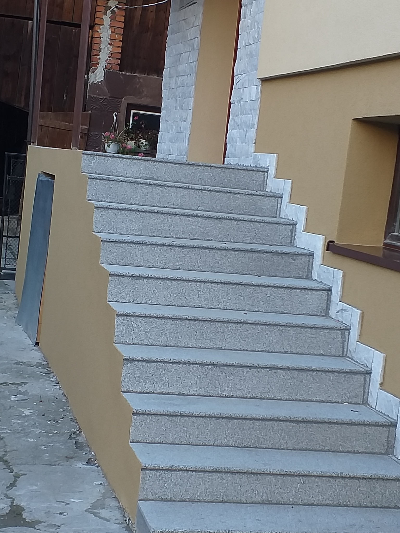 Zewnętrzne schody wykończone szarą kostką brukową prowadzące do budynku z ocieploną elewacją w kolorze beżowym, z widocznymi fragmentami białego kamienia dekoracyjnego.