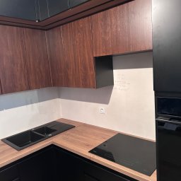 JEL-TOMIX TOMASZ CIURA - Nowoczesna kuchnia z drewnianymi szafkami górnymi i czarnymi dolnymi. Na blacie czarny zlew i płyta indukcyjna. Na ścianie notatki z wymiarami.