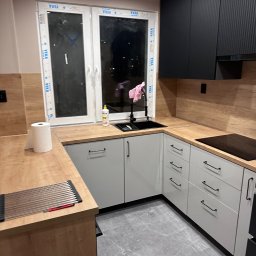 JEL-TOMIX TOMASZ CIURA - Nowoczesna kuchnia z szarymi szafkami, drewnianym blatem i czarnymi akcentami. Widoczne okno z naklejkami, zlewozmywak i płyta indukcyjna. Minimalistyczny design.