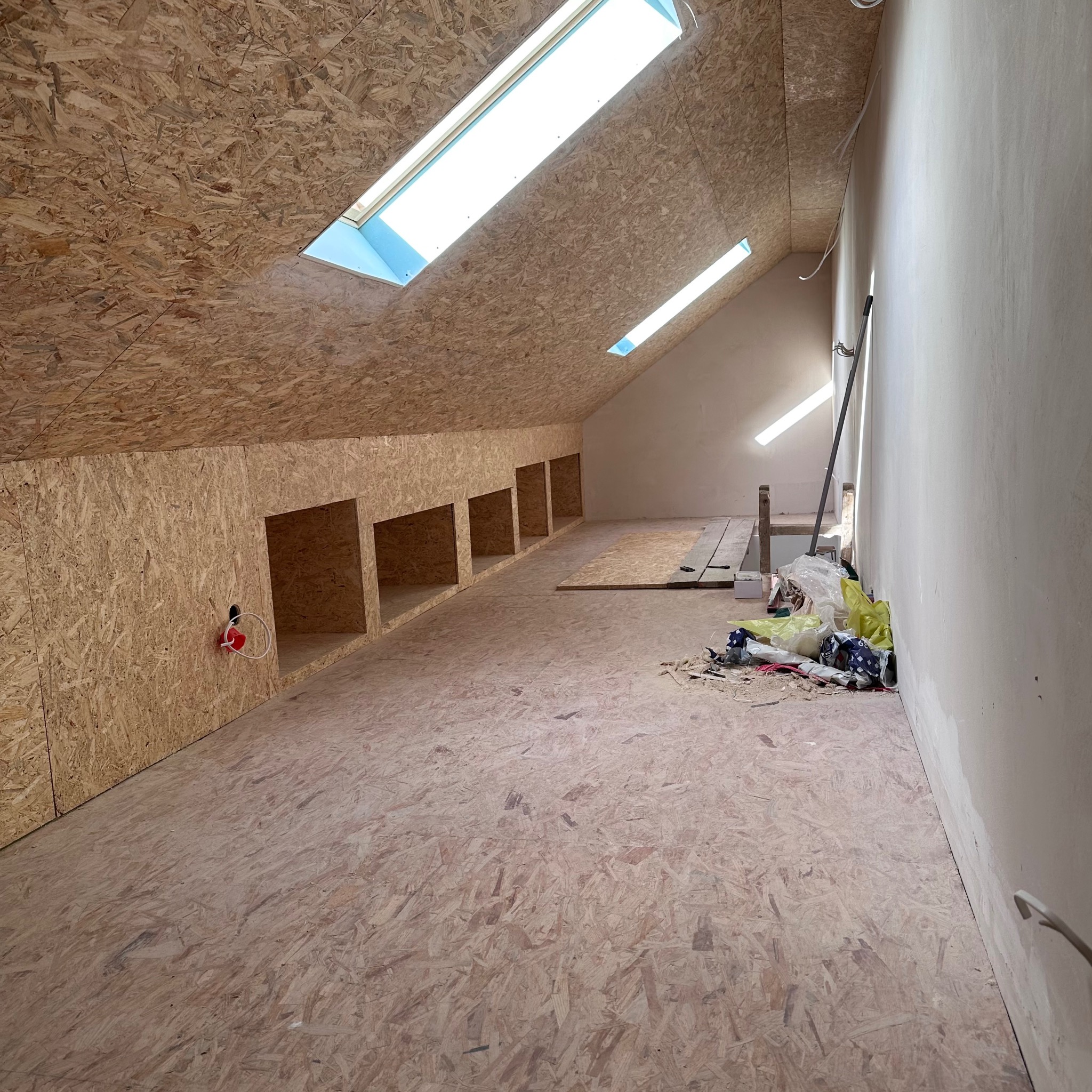 Adaptacja poddasza: ściany i sufit wyłożone płytą OSB, wbudowane wnęki, okna dachowe w skosach. Widoczne ślady prac wykończeniowych.