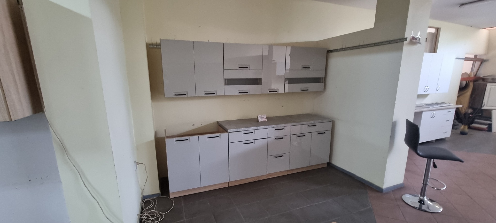 Szare szafki kuchenne z ciemnymi uchwytami, widoczne kable na podłodze, pomieszczenie w trakcie wykańczania.