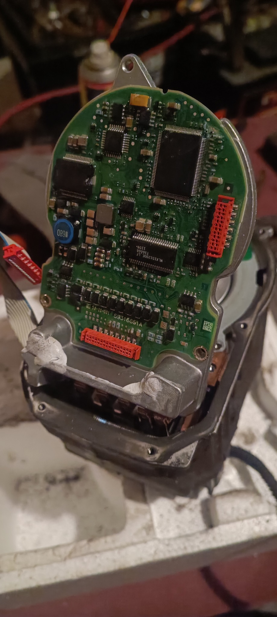 Otwarty moduł sterujący z widoczną zieloną płytką drukowaną, z czerwonymi złączami i elementami elektronicznymi. Widoczne ślady naprawy/lutowania na obudowie.