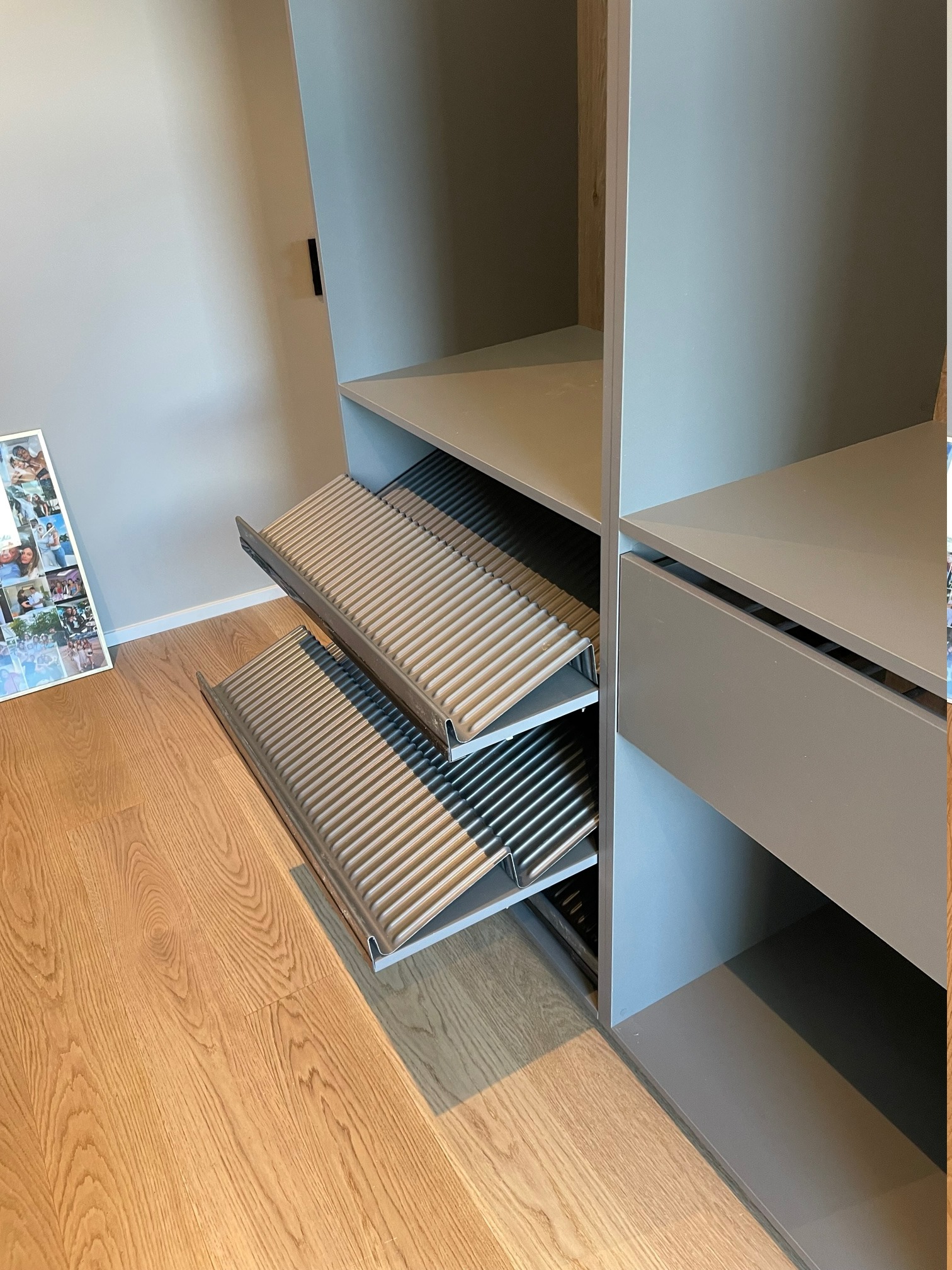 Wysuwane półki na buty w szafie na wymiar, widoczne dwie półki z metalowymi prętami, szara obudowa szafy, parkiet na podłodze.