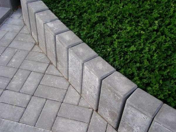 Szara nawierzchnia z kostki w jodełkę, obrzeże z trapezoidalnych betonowych elementów, obok rabata z zielenią, Bydgoszcz.