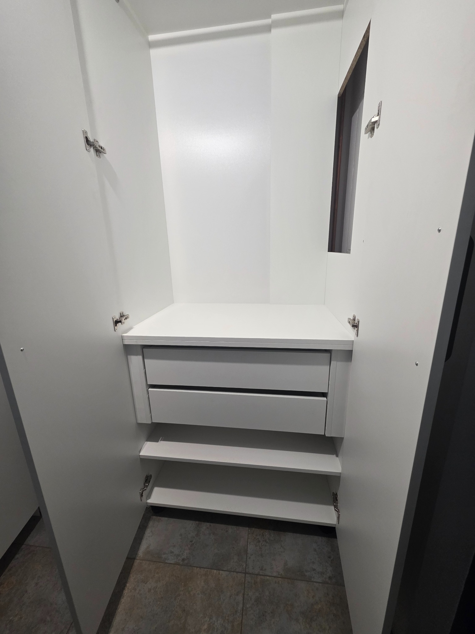 Wnętrze białej szafy z otwartymi drzwiami, widoczne dwie szuflady i trzy półki w dolnej części.