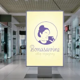 Ilustracja logo Bonasavine umieszczona na podświetlanym billboardzie wewnątrz centrum handlowego. Logo przedstawia uproszczony rysunek kobiety robiącej selfie, umieszczony w okręgu, nad napisem...