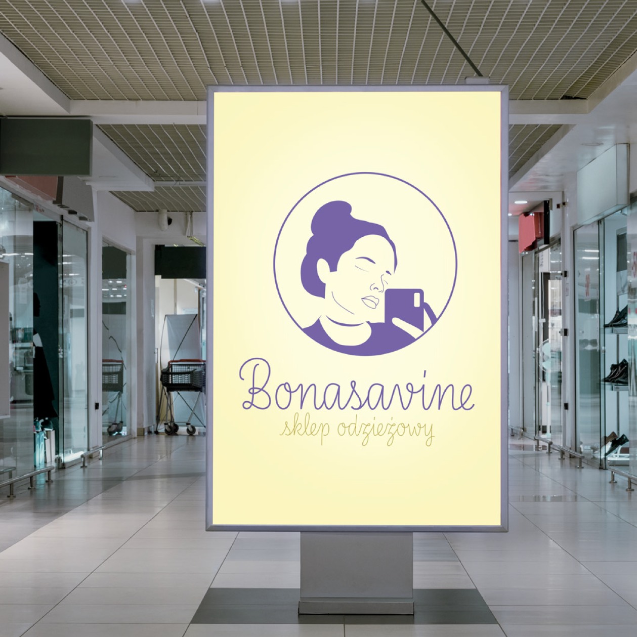 Ilustracja logo Bonasavine umieszczona na podświetlanym billboardzie wewnątrz centrum handlowego. Logo przedstawia uproszczony rysunek kobiety robiącej selfie, umieszczony w okręgu, nad napisem...