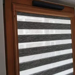 Roleta dzień noc w drewnianej ramie okiennej, z czarną kasetą i łańcuszkiem sterującym po lewej stronie.