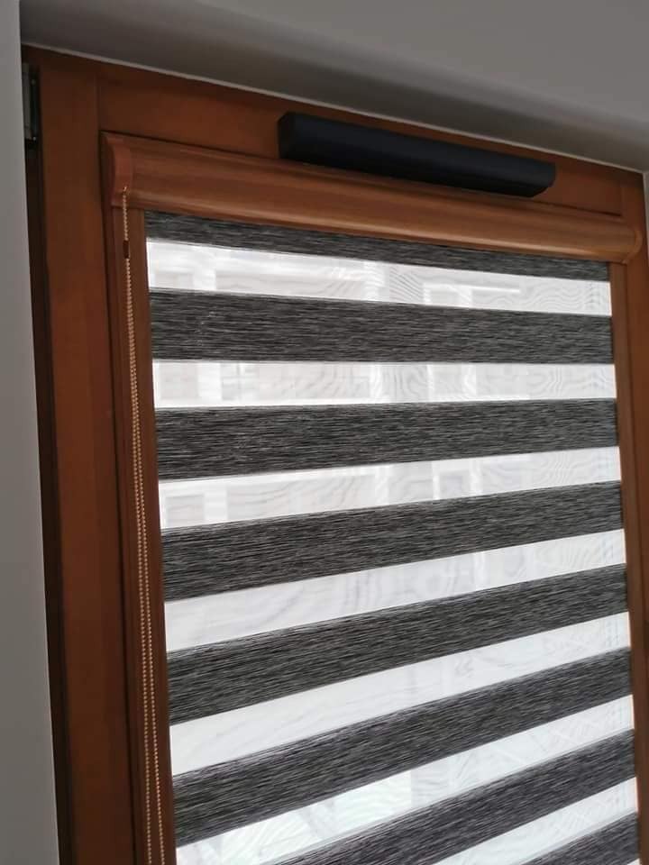 Roleta dzień noc w drewnianej ramie okiennej, z czarną kasetą i łańcuszkiem sterującym po lewej stronie.