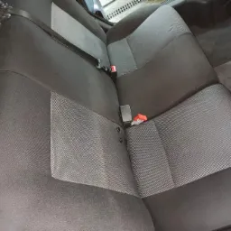 Czarne i szare tylne siedzenie samochodu z widocznymi pasami bezpieczeństwa i elementami mocującymi.