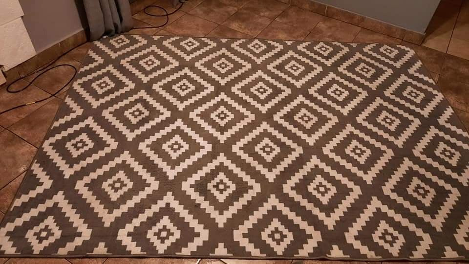 Brązowo-beżowy dywan z geometrycznym wzorem rombów na brązowej podłodze z płytek ceramicznych.