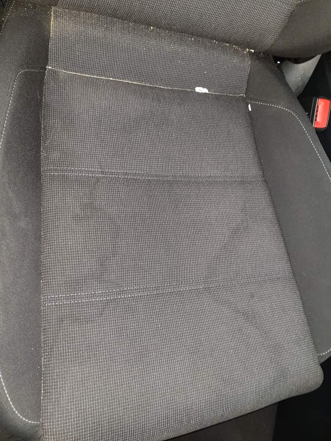 Szare tekstylne siedzenie samochodowe z widocznymi zabrudzeniami i okruchami w górnej części oparcia.