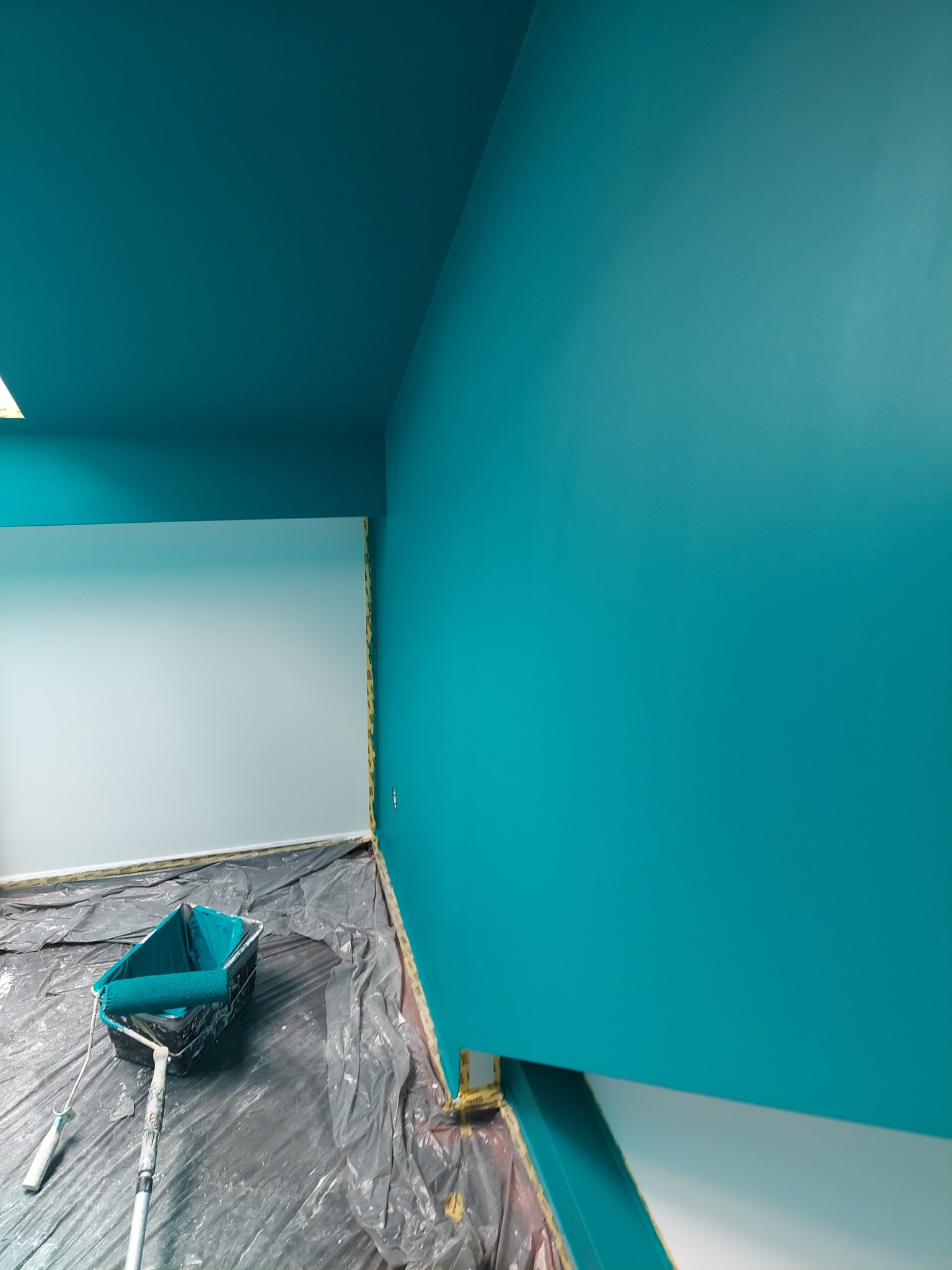 Świeżo pomalowane na turkusowo ściany i sufit w pomieszczeniu w Gliwicach, z widocznym wałkiem i kuwetą malarską na folii ochronnej.