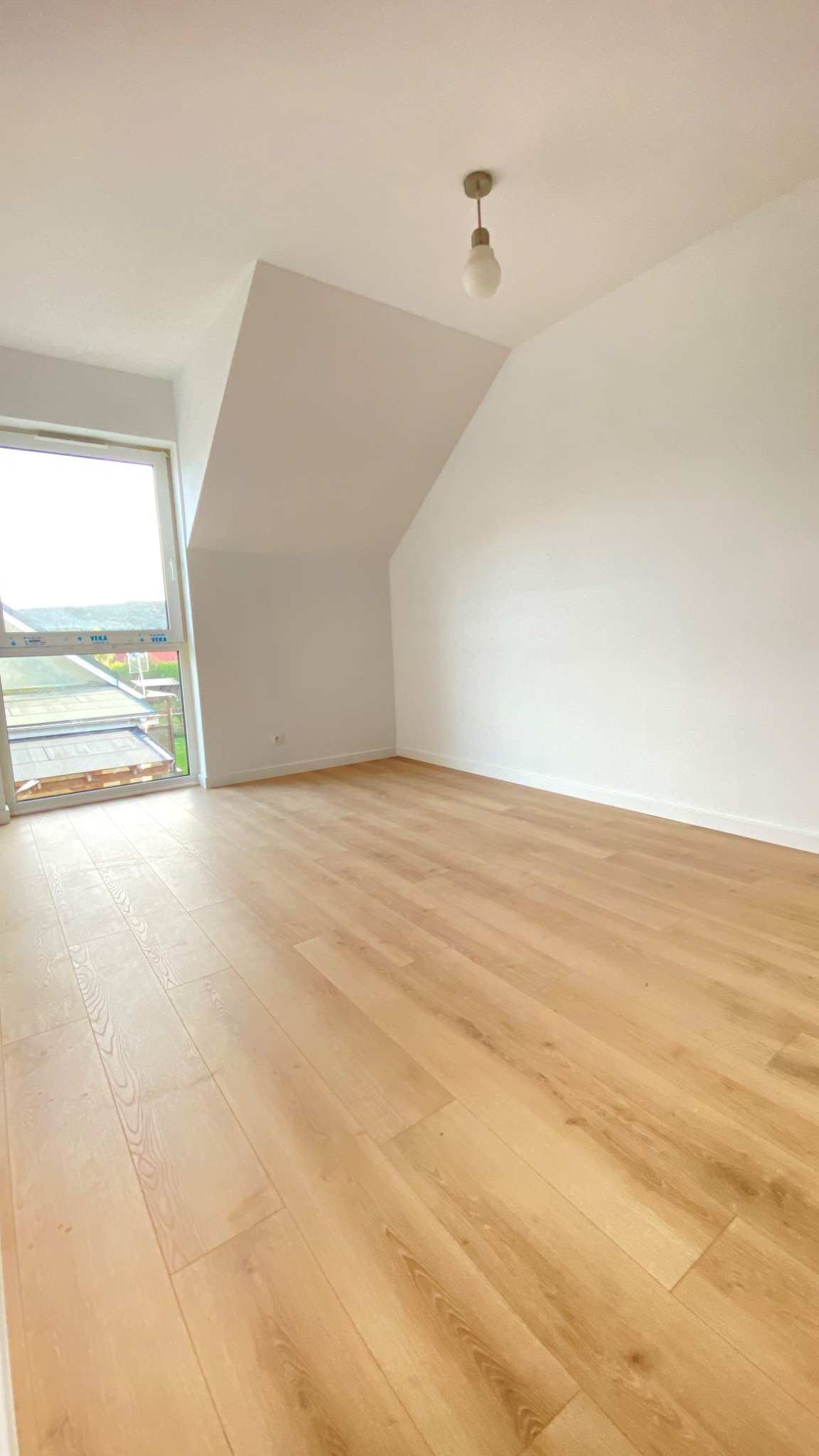 Poddasze po remoncie z jasną podłogą panelową, białymi ścianami i oknem z widokiem na zewnątrz.